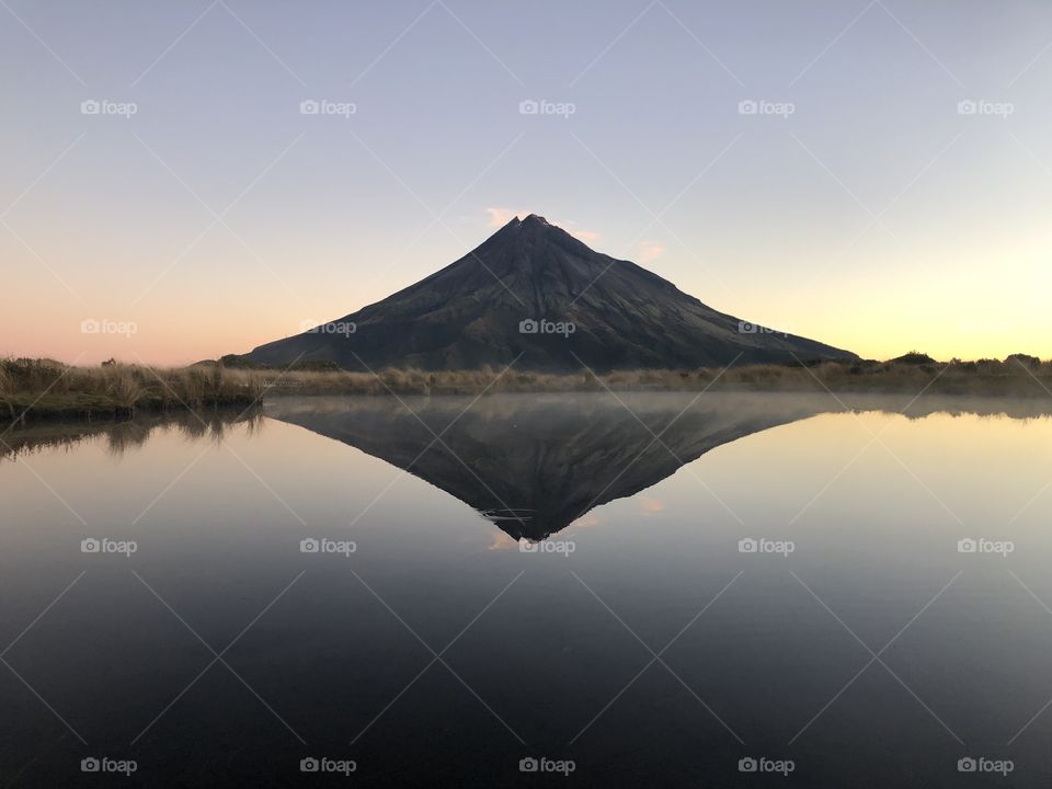As the wind calms and the sun sets, a beautiful reflection of Mt Taranaki is reflected on the lakes surface