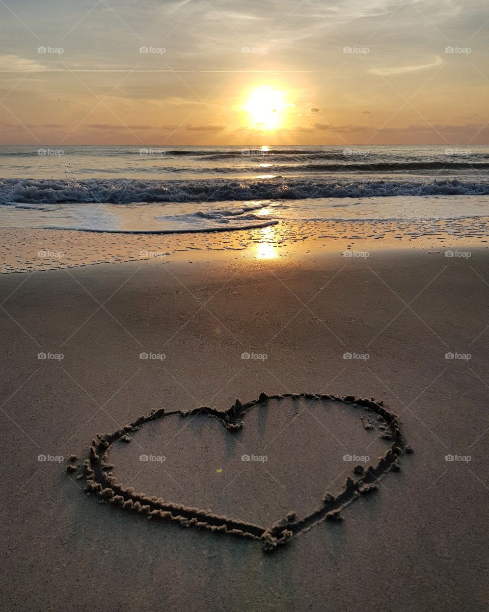 Heart on beach against sunrise sky
