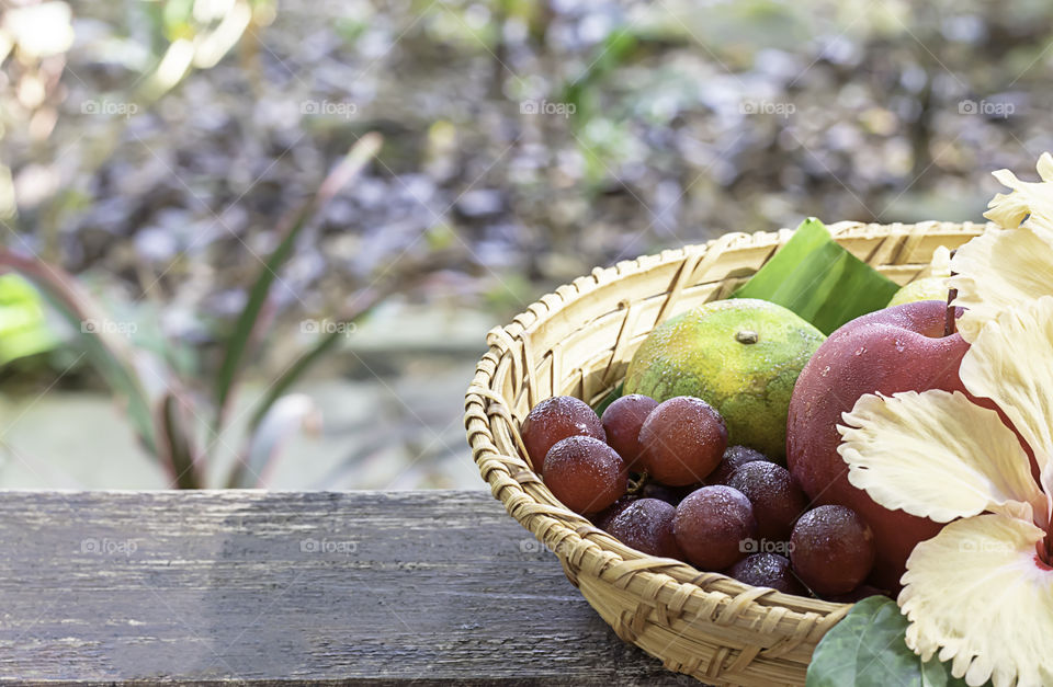 Apple, Orange and grape in weave bamboo baskets with floral decorations Background blurry trees.