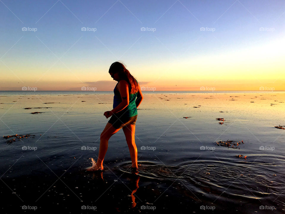 Young girl wading  in ocean at low tide at sunset 