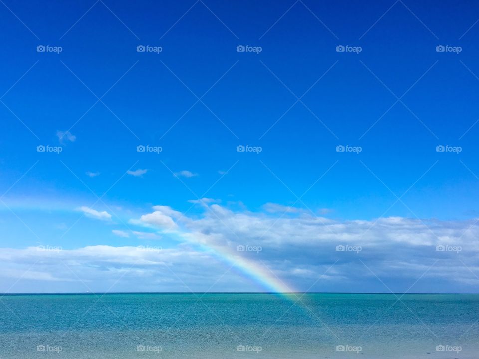 Bright rainbow over ocean illuminating translucent into the water