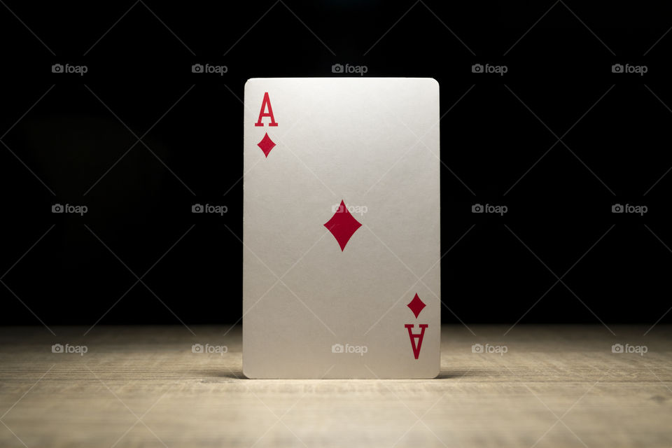 A close up portrait of a diamond ace card standing up in a spotlight on a wooden table. the playing card is emerging out of the darkness.
