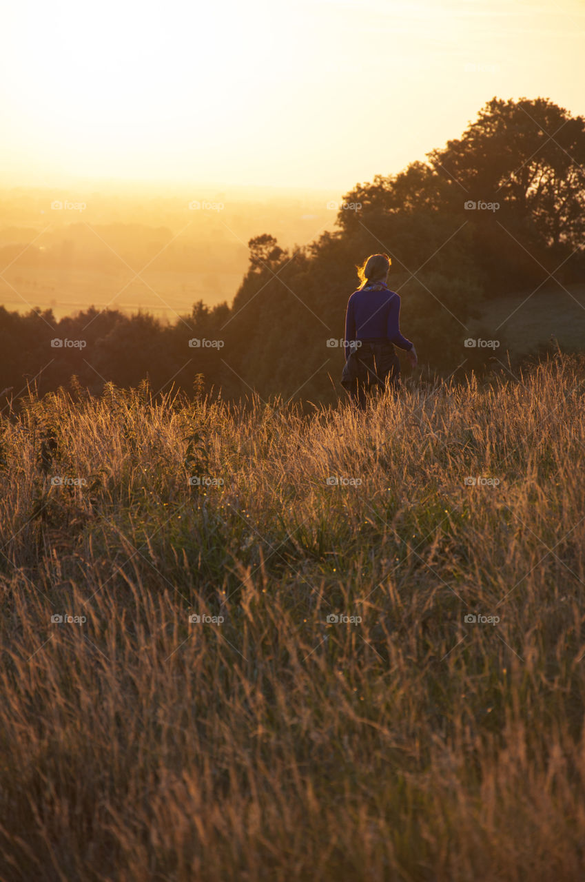 girl walking in golden fields of Glastonbury hill during sunset