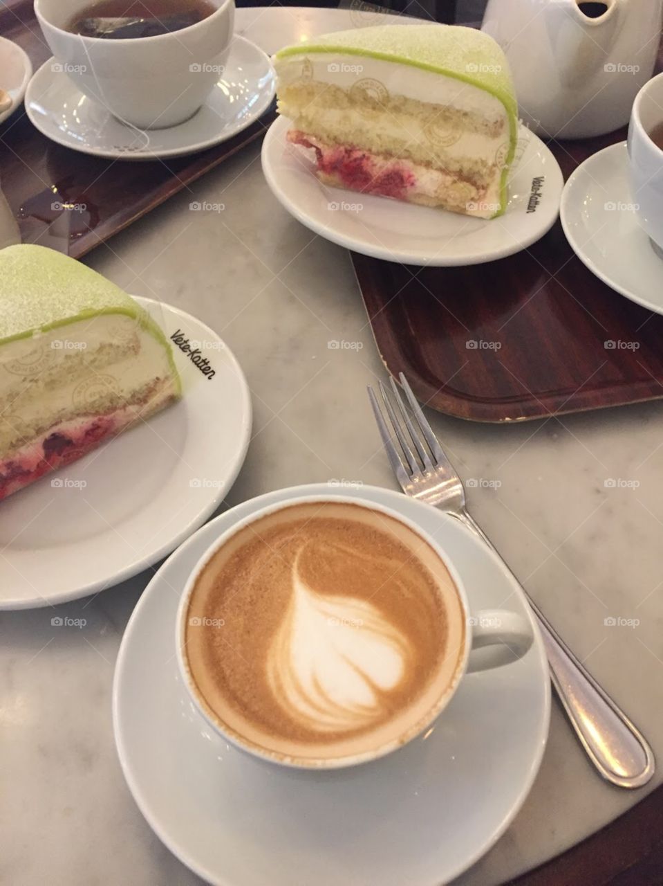 Cappuccino next to two slices of princes cake- green cake with layers of angel food, cream, and raspberry. 