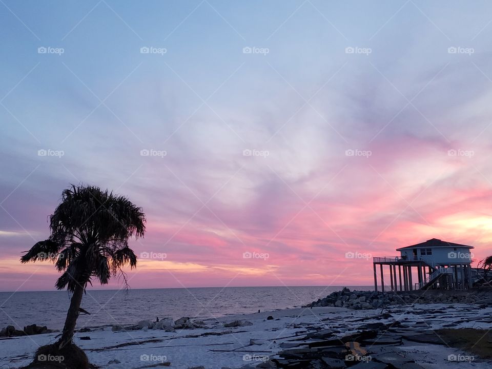 sunset on a florida gulf beach with palm tree and house