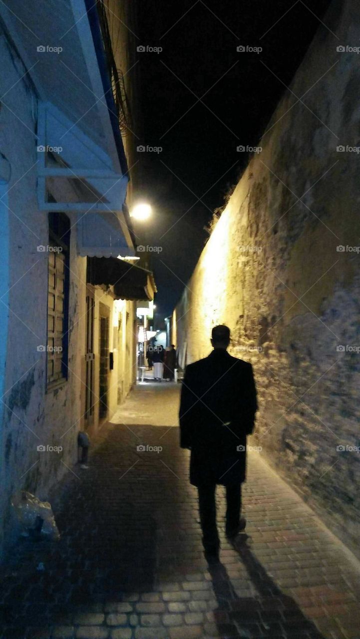 One adult man walking in the street at night at essaouira city in Morocco.