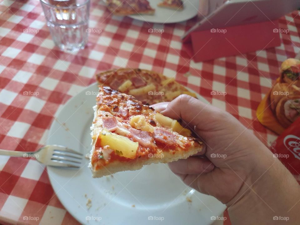 a close up portrait of someone holding a slice of pizza with pineapple in one hand.