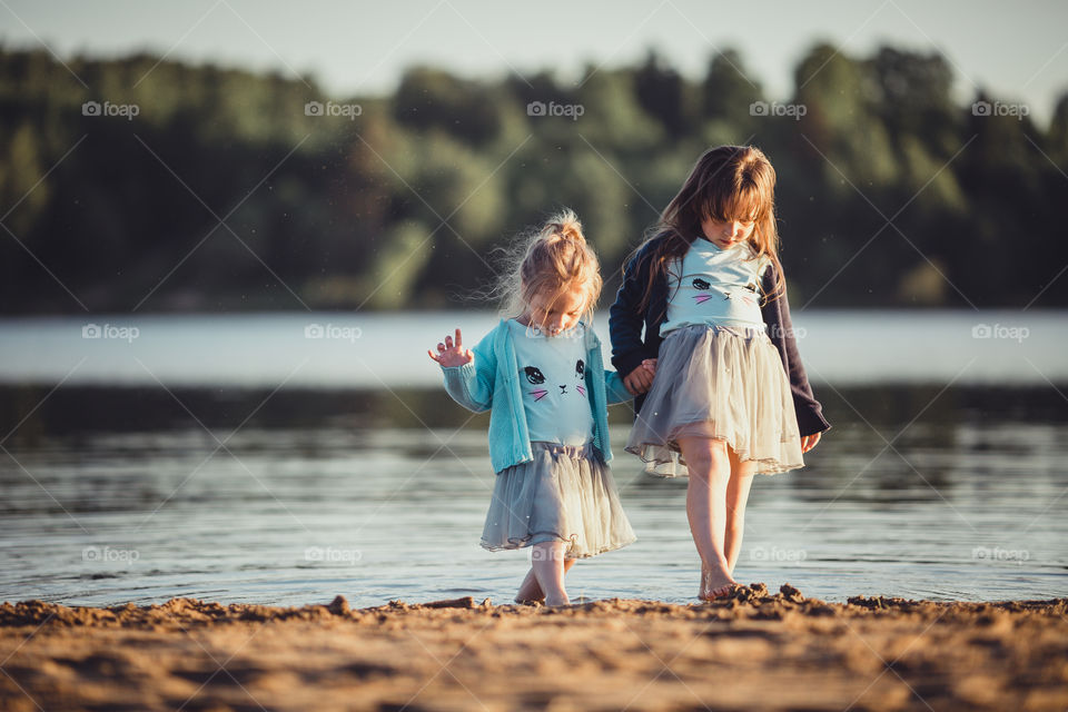 Little sisters on lake coast at sunny evening. 