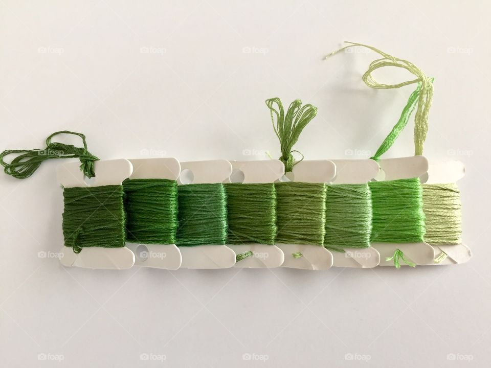 Green Color Story - flat lay of various shades of green embroidery floss / cross stitch thread on paper spools arranged horizontally by hue