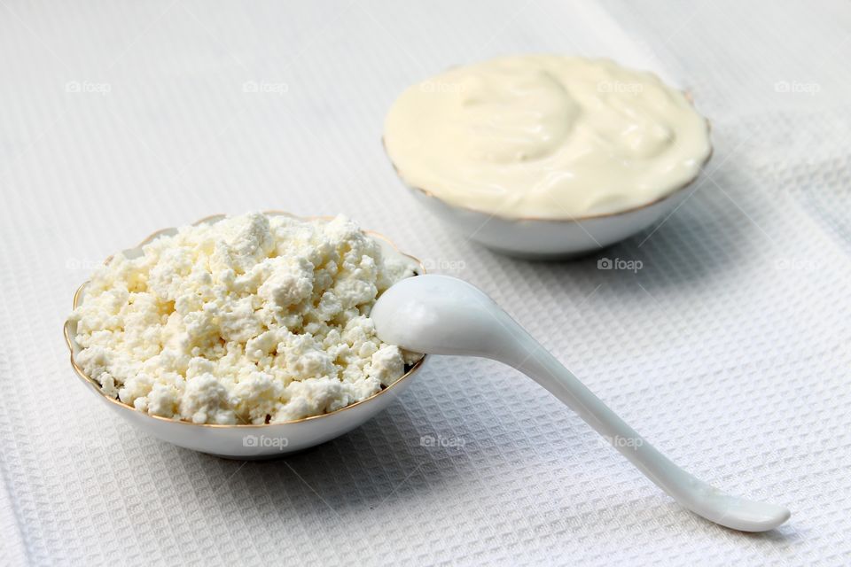natural milk products: cottage cheese and sour cream appetizingly arranged diagonally in small porcelain white plates, top view