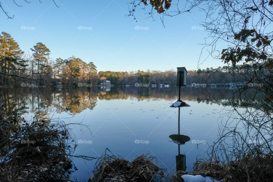 A wood duck box with a patch of snow in the millpond with the old mill visible in the background at Yates Mill County Park in Raleigh North Carolina. 