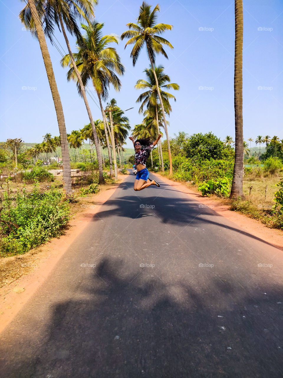 young woman jumping in the air in an open road with palm trees on both sides