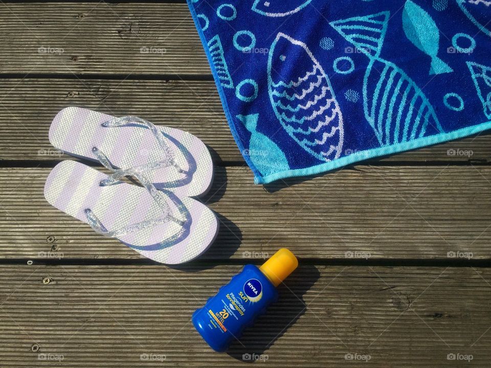 Flat lay summer items on wooden deck: flip flops, towel and Nivea sunscreen