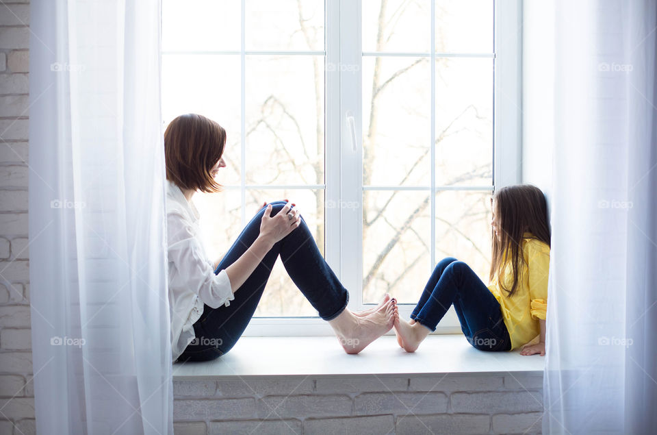 Mother and daughter sitting on windowsill