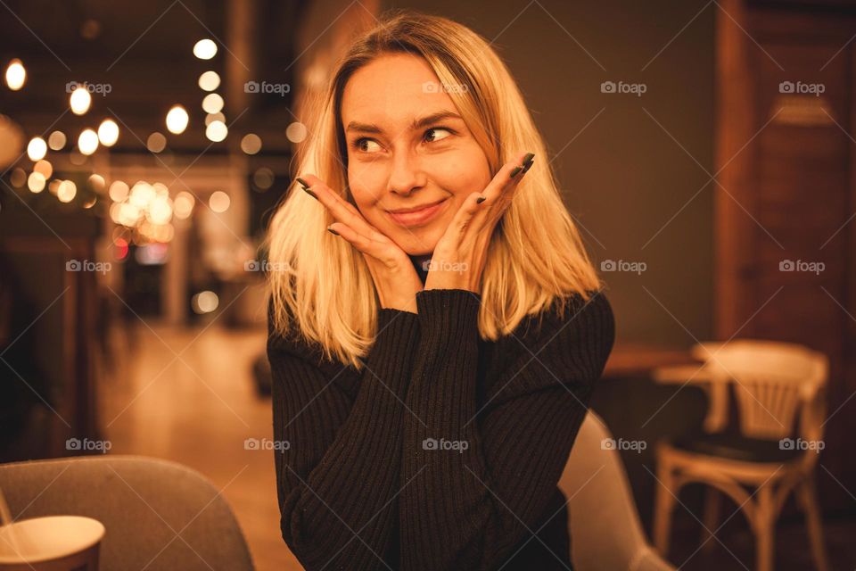 Young woman sits in a cafe.Happy blonde is resting in a cafe. Portrait photo of a woman in a black sweater