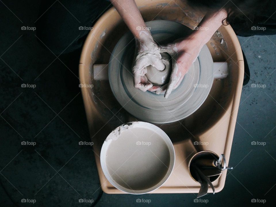 Unrecognisable ceramist working on a potter's wheel in a ceramic studio, top view