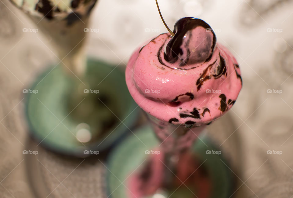 Gourmet pink ice cream melting with floating dark cherry covered in dark chocolate sauce 