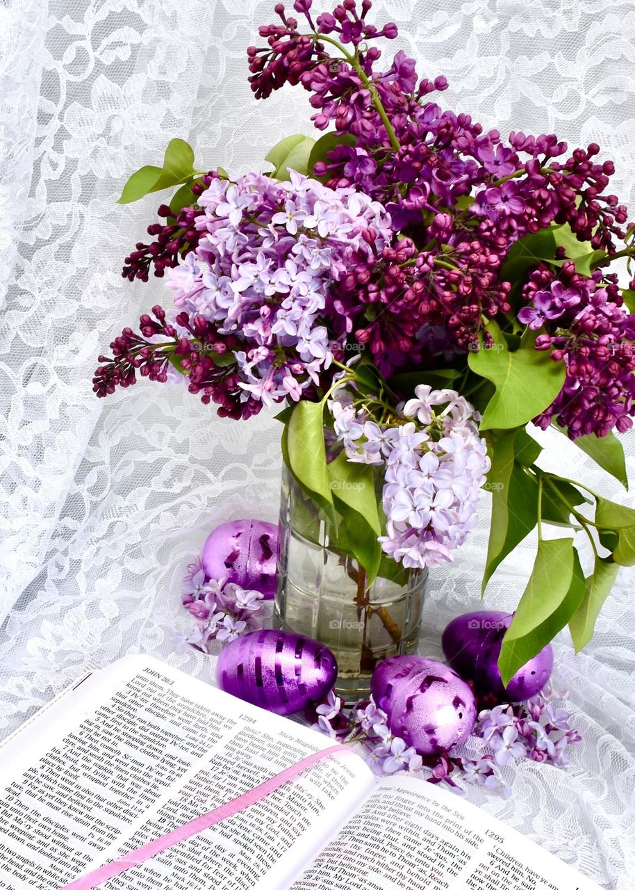 Springtime lilacs in a vase with purple Easter eggs and an open Bible 