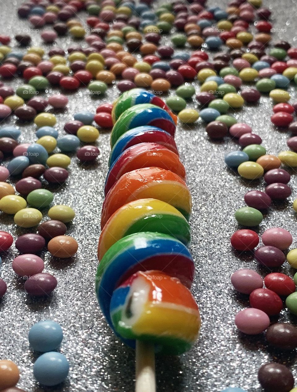 A rainbow coloured lollipop surrounded by colourful sweets