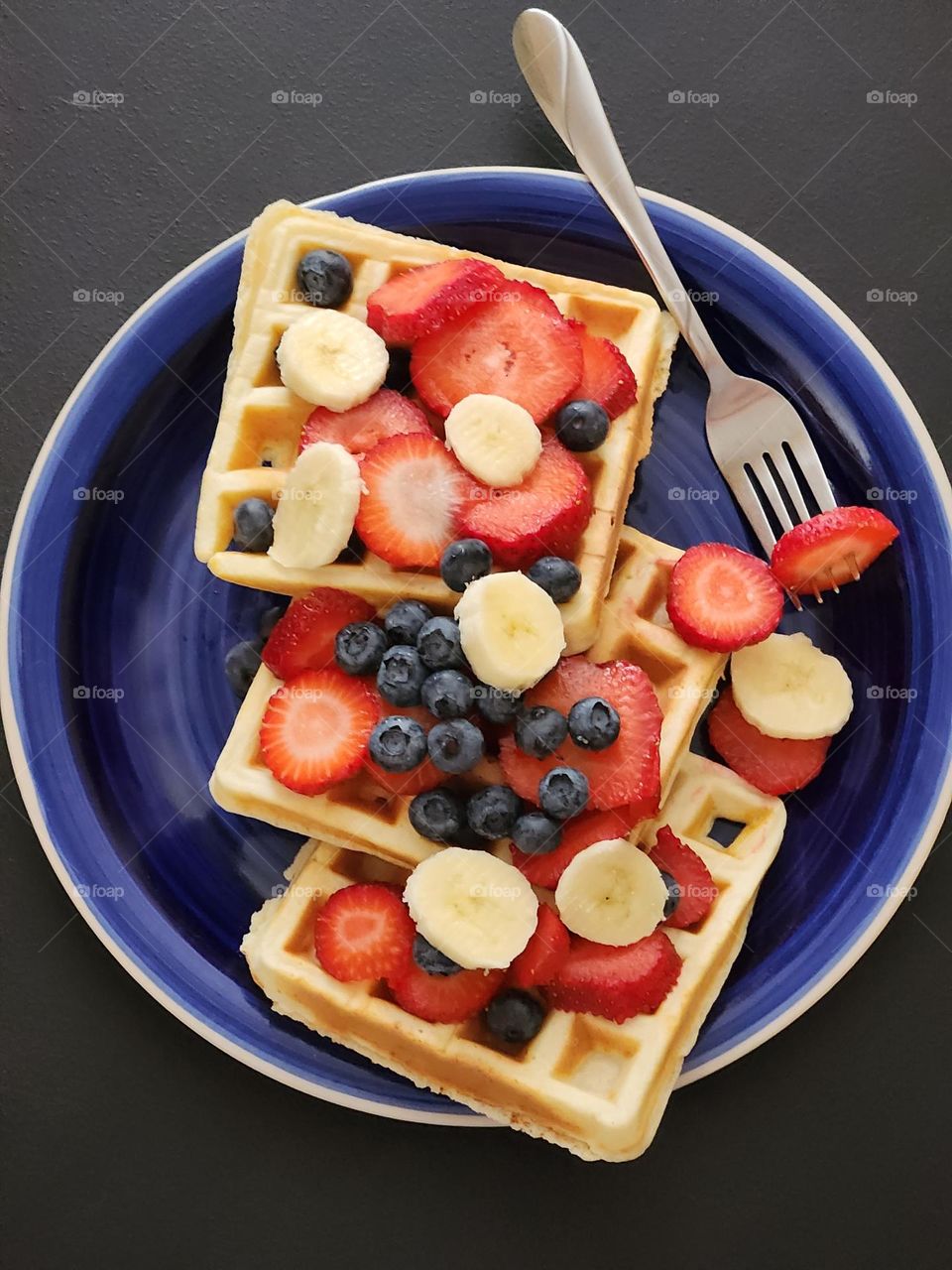 Home-made waffle breakfast, with red, white, and blue fruit on a blue plate, in celebration of The 4th of July holiday