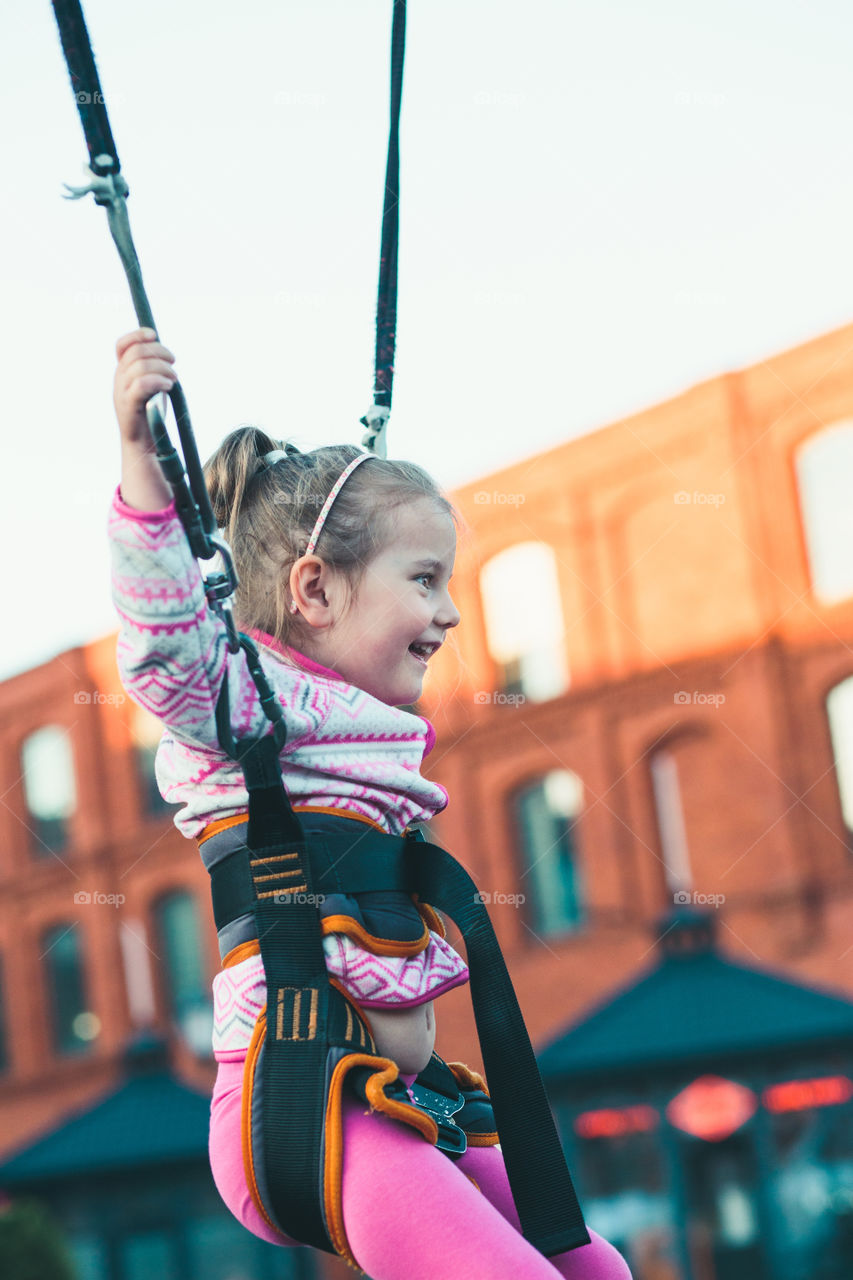 Little adorable smiling girl jumping on trampoline, having fun at funfair