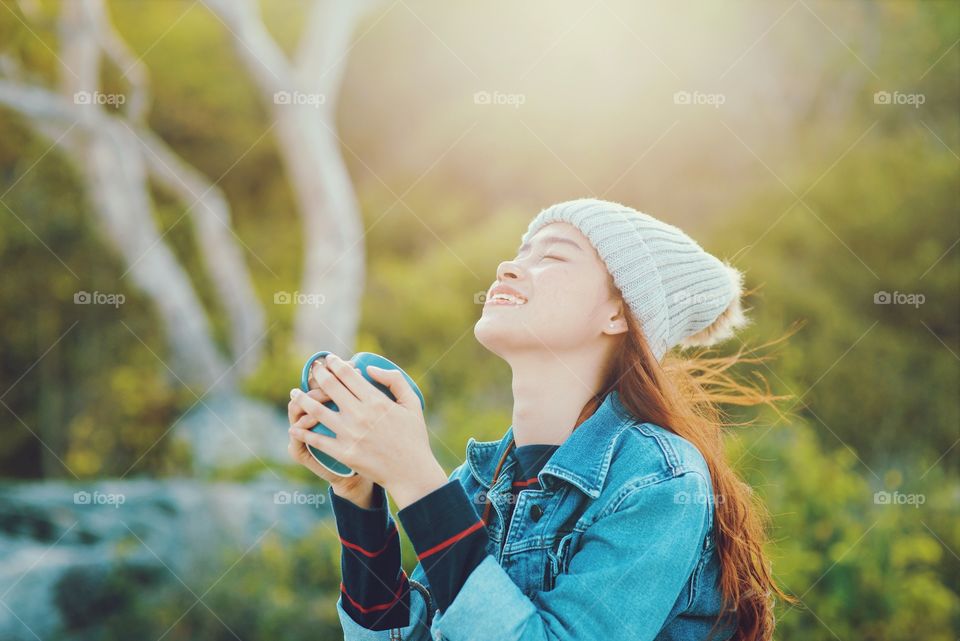 Happy Asian woman holding coffee cup in nature.