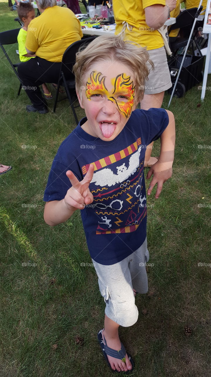 boy with face paint giving peace sign stocking tongue out