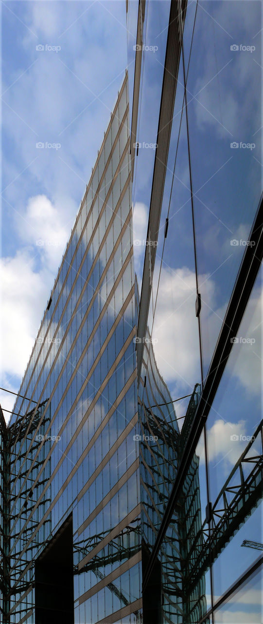 Low angle view of modern skyscraper reflecting cloudy sky in Berlin, Germany.