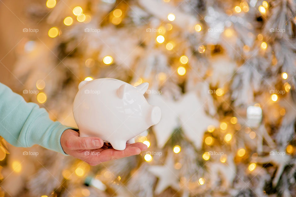 piggy bank with 100 dollars banknote in festive New Year atmosphere of scenery.  Magical bokeh with Christmas tree and bright lights.