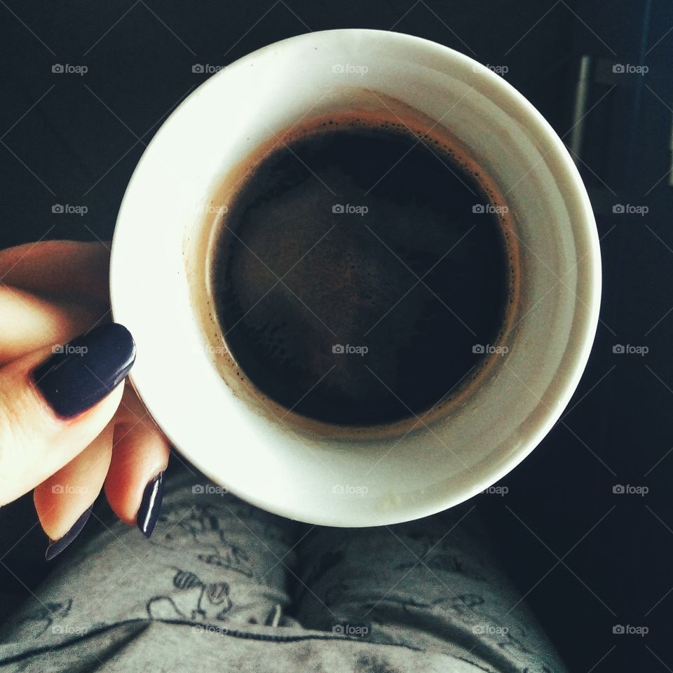 Woman's hand with purple manicured nails holding a cup of coffee