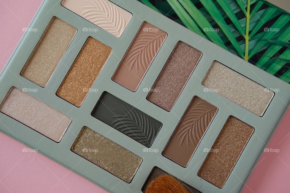 Directly above view of eyeshadow pallet in earth tones against pink background. 