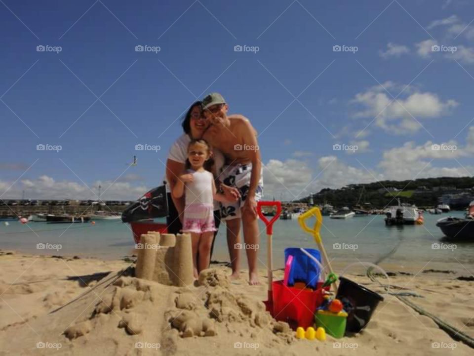 family photo on st ives beach,
with sandcastle ,
blonde, Caucasian little girl , man, woman , parents and daughter . looking forwards , St. Ives , cornwall, South,  West,  of, England,  United Kingdom,  of, great Britain,  
summer time, sunshine