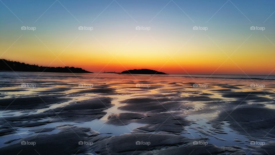 colorful reflections. a bright orange sunrise reflects on the quite beach