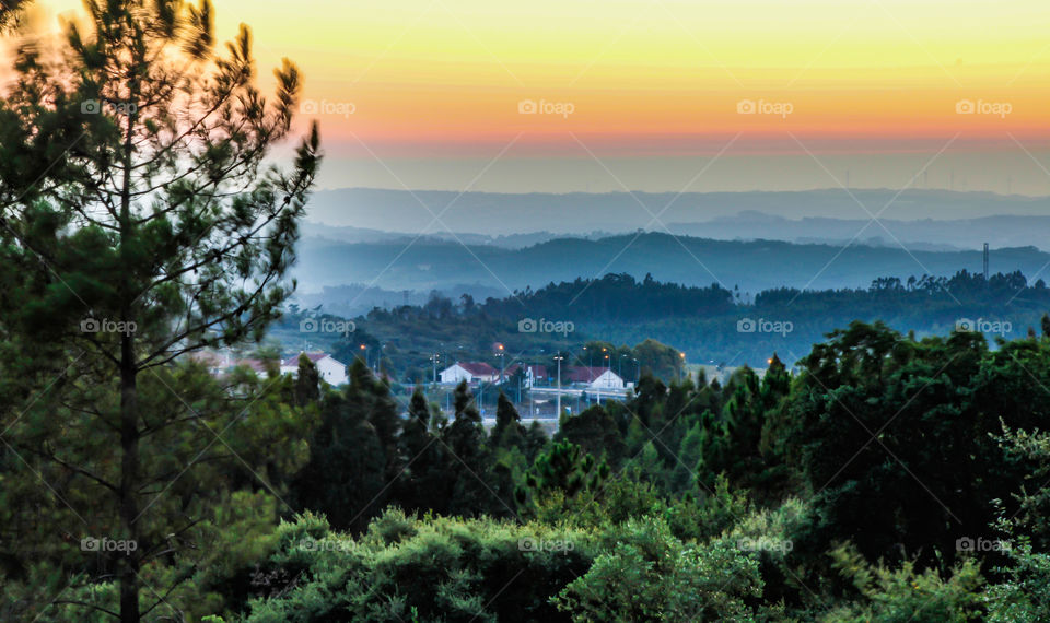 Landscape after sunset, trees cover hills are hazy under the orange sky