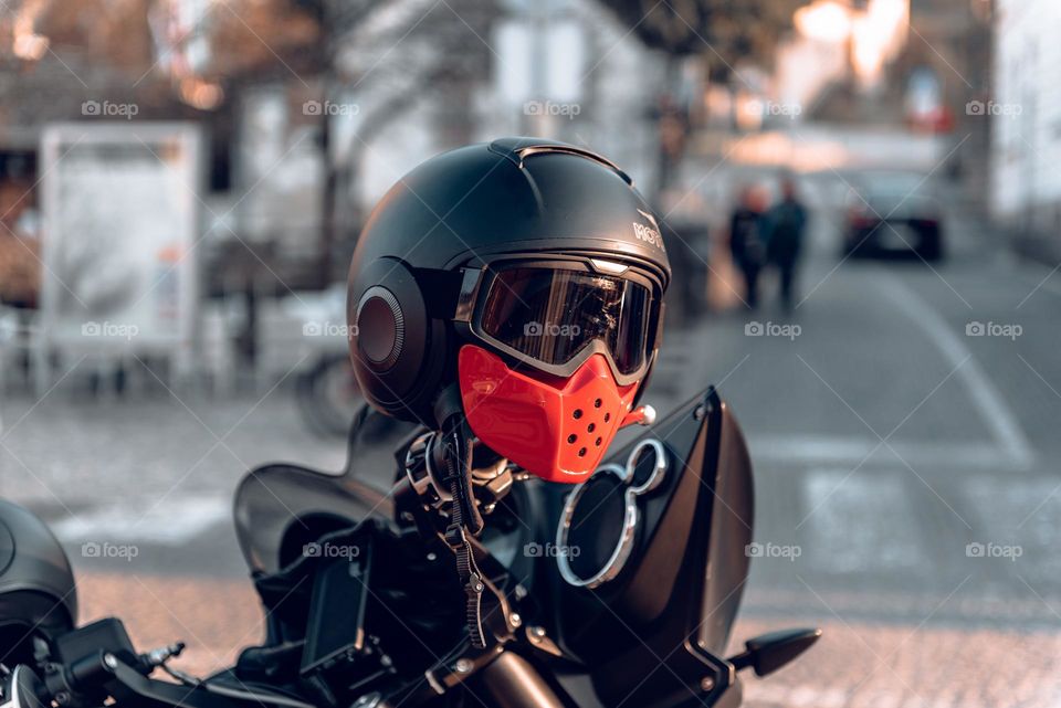 Close-up photo of black helmet on motorcycle handlebars in city