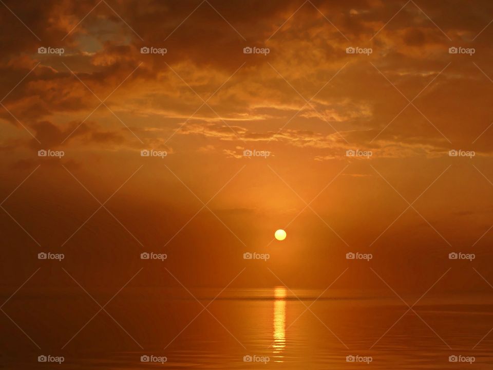 A mystical orange sunset surrounded by in coming fog. The descending sun reflected upon the shimmering waters surface