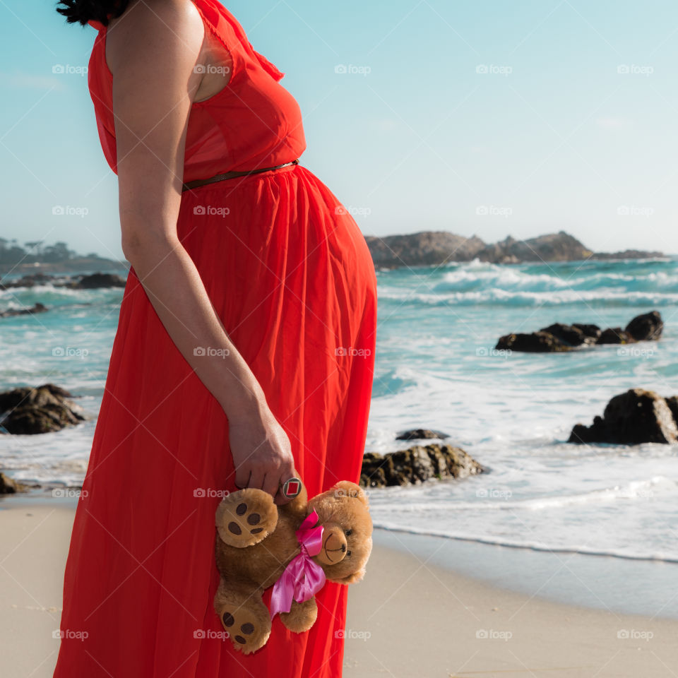 Pregnant woman in red dress standing by the ocean