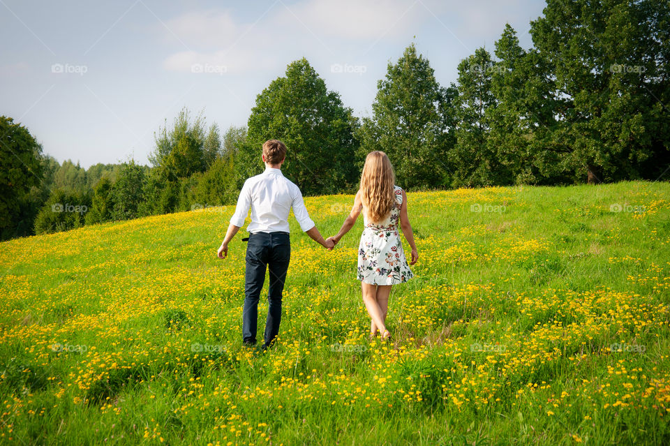 Love is in the air. Young happy couple holding hands in a meadow full of yellow wildflowers.