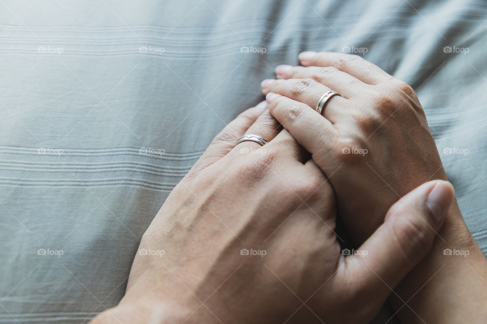 Close up husband and wife hands together on gray beds and beautiful wedding rings