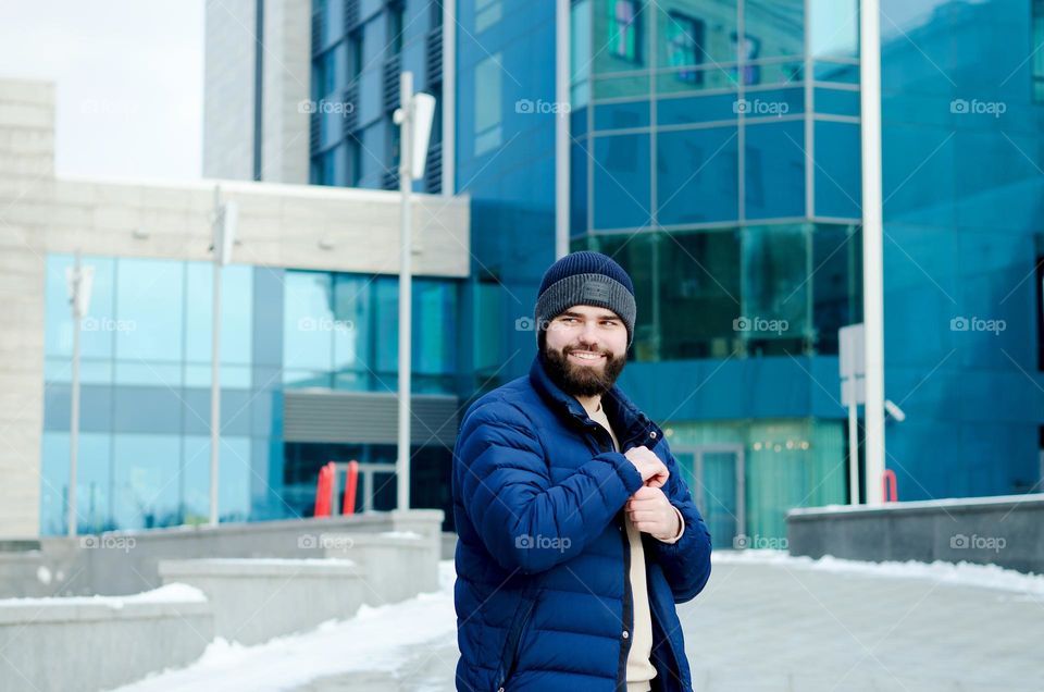 Portrait of happy, smiling, friendly bearded young man in casual clothes walking in city street in winter. Ukraine