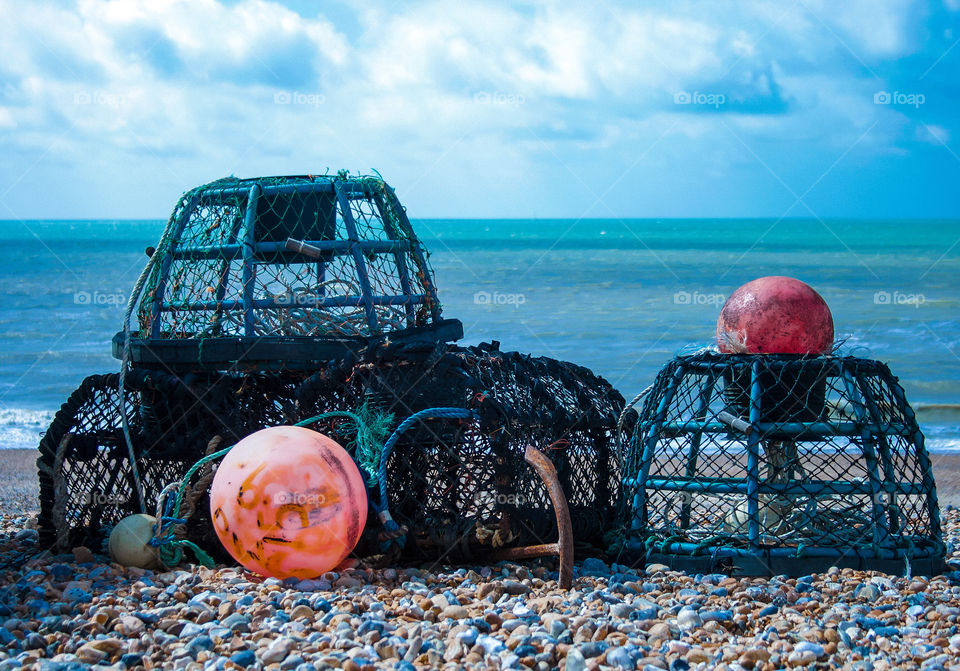 Lobster/crab pots sit with orange buoys on Hastings pebbled beach, the English Channel in the background