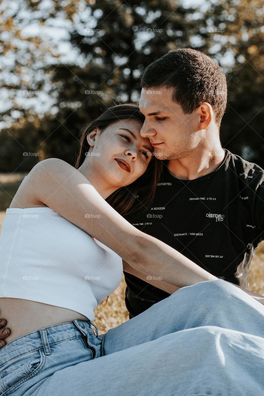 One beautiful young caucasian couple sits in an embrace, the guy lovingly and tenderly looks at his girlfriend, close-up side view. Concept moment of happiness, romantic picnic.