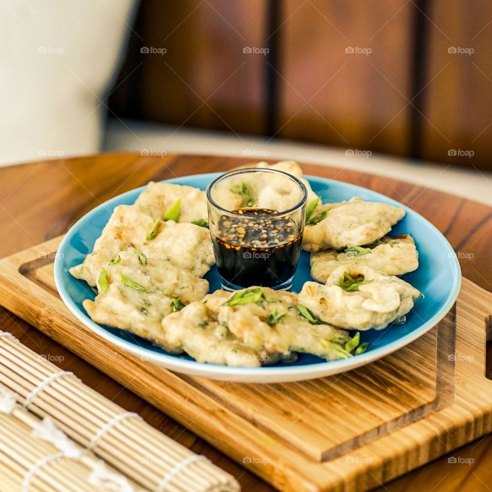 Fried tempeh sprinkled with chopped green onions combined with soy sauce sauce. Plate. Tempeh. Glass. Table. Wood. Wood motif. Café. Cutting board. Snack. Eat. Food. Fried food. Crispy. Photography.