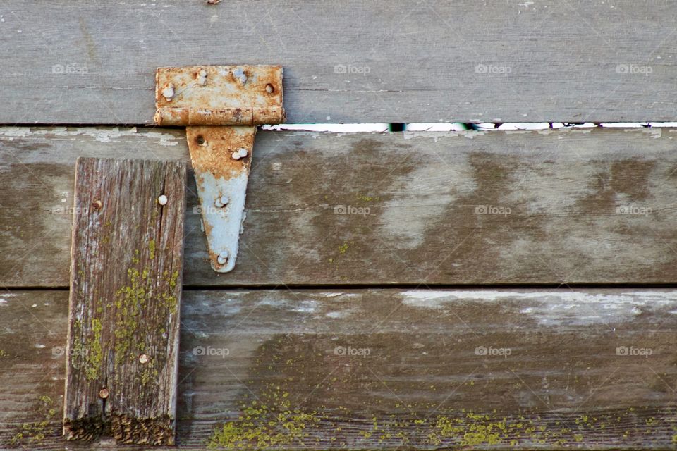 Rusted hinge on a weathered wooden ventilation opening in the siding of an antique farm building  