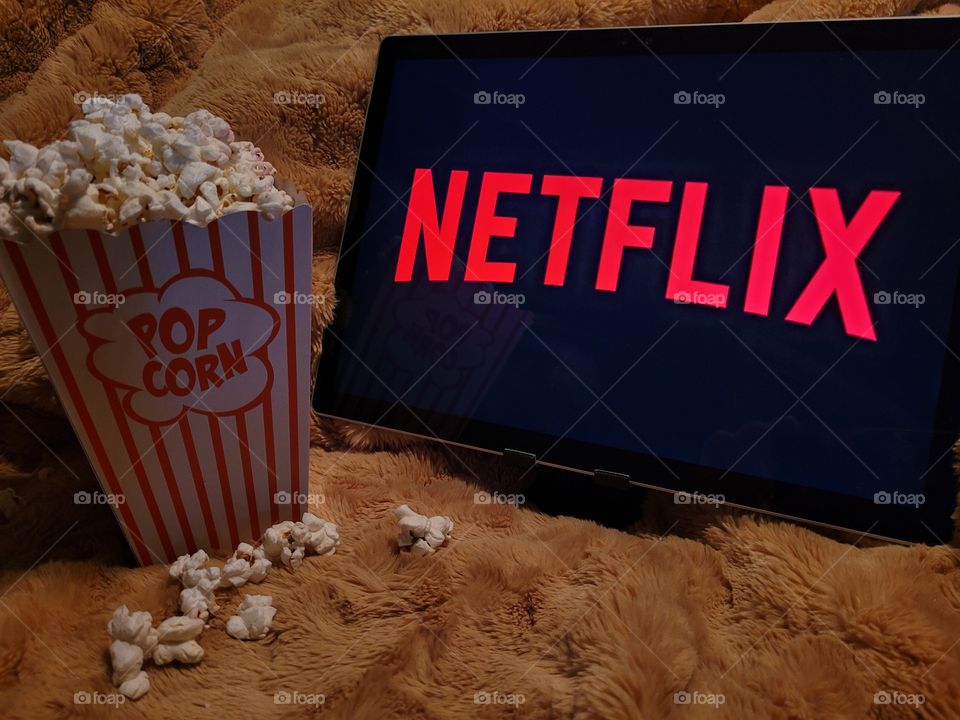 Laptop computer screen ready to watch Netflix for a fun, cozy, and relaxing night with popcorn as a snack, on soft bed blanket in dark room