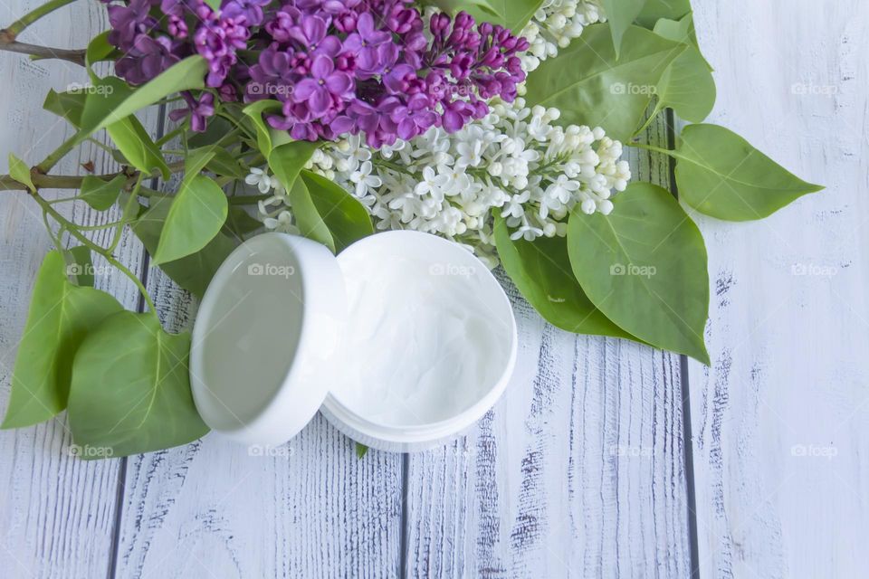 Spring, white and purple, fragrant lilac with green leaves and jars with cosmetic cream and product.