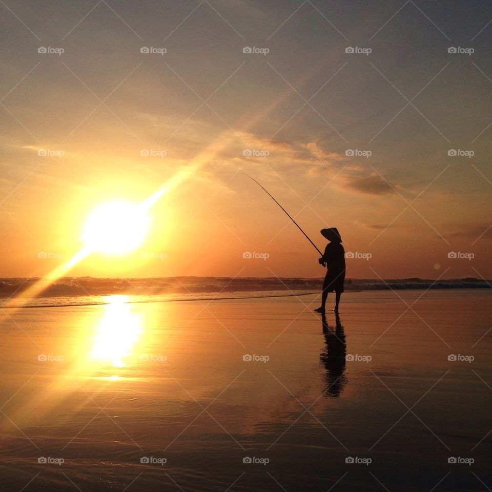 Silhouette of man fishing in sea at sunset