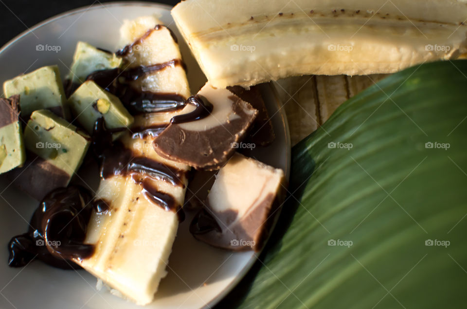 Dark chocolate sauce covered split banana with leaf and banana and matcha green tea fudge confections for gourmet hot sundae toppings or sweet treat conceptual healthy dessert background 