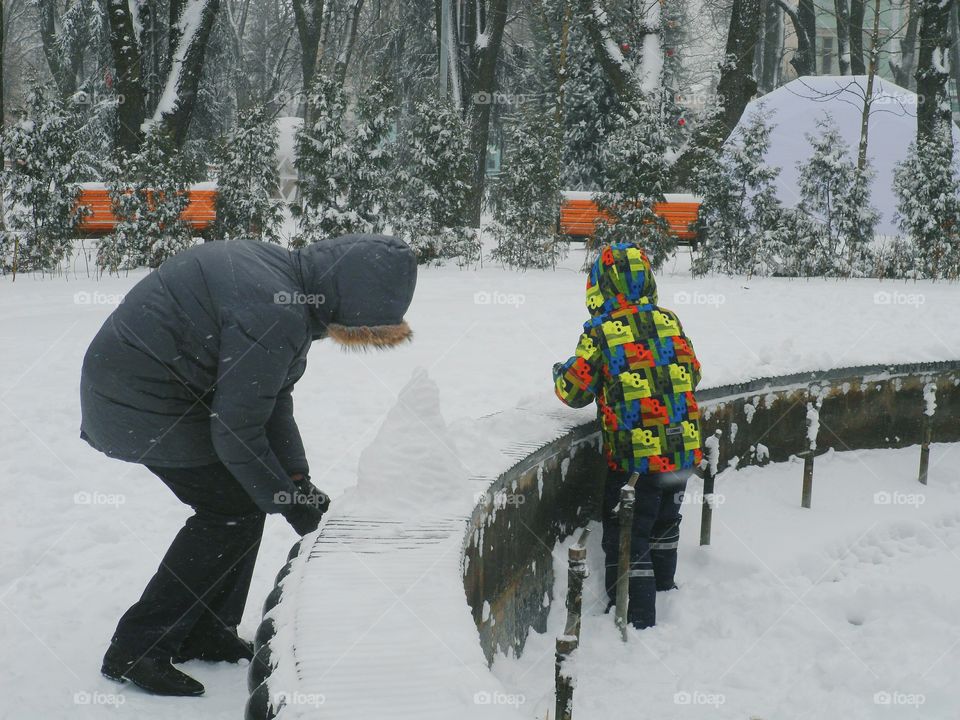 man and child sculpt a snowman in the park, Kiev, winter