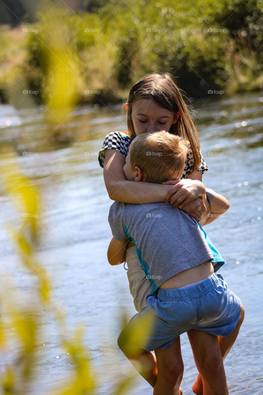 Brother and sister hugging and sharing the love alongside the river on a hot summer day